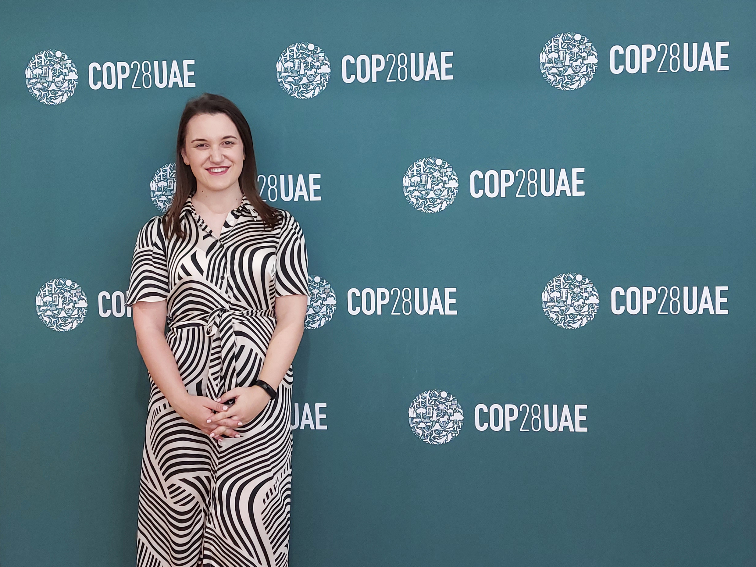 Megan Yeates, WorldSkills Kazan 2019 gold medallist in Freight Forwarding, standing in front of a COP28 billboard at the COP28 event in Dubai.