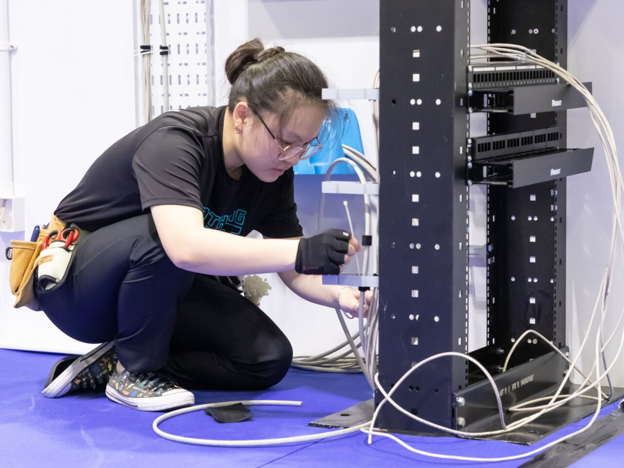 A Competitor in Information Network Cabling kneeling in front of cable casing holding wires during the WorldSkills ASEAN 2023 Competition held in Singapore in July 2023.