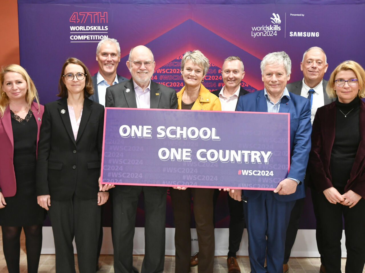 Representatives from WorldSkills International and WorldSkills Lyon 2024 stand with a poster for official launch of One School One Country in Lyon, France